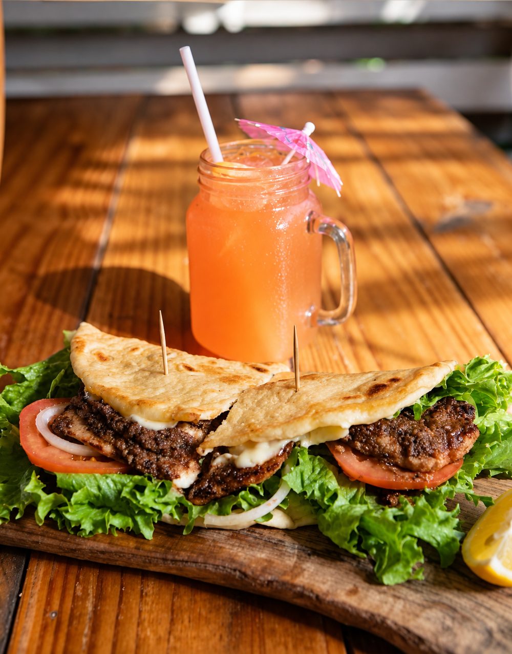 A folded flatbread with meat, lettuce and onion, and a mason jar of a pink iced drink with a paper umbrella.