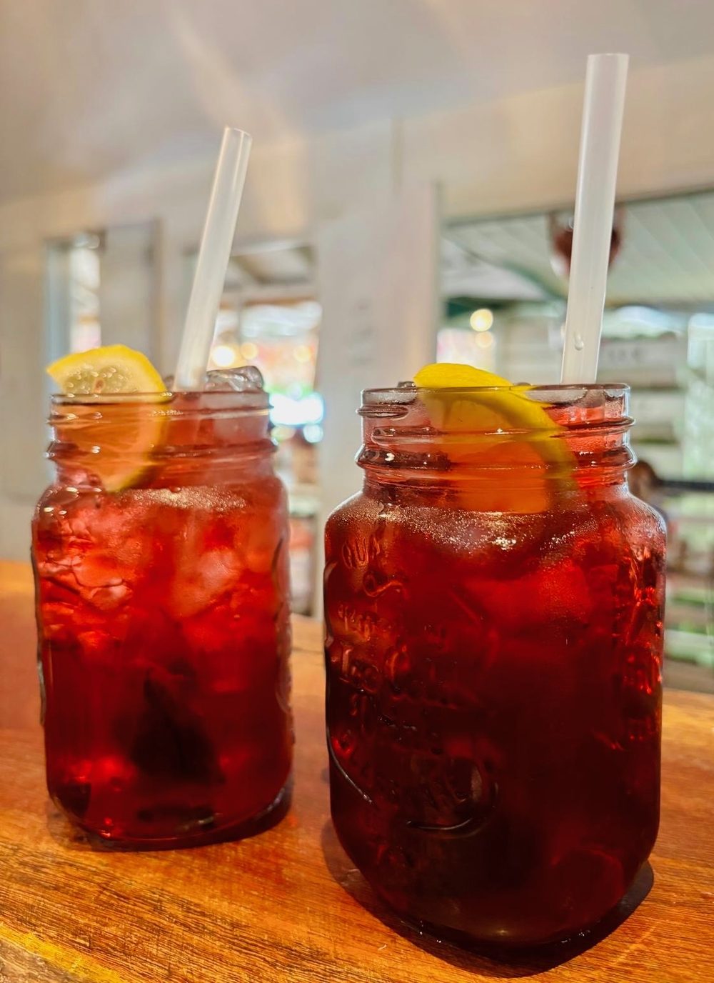 Two mason jars of deep red iced drinks with lemon slices and straws.